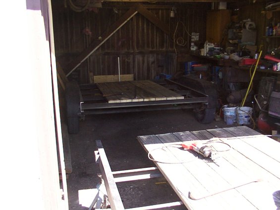 Two trailers, one with wooden planks and a grinder, sit in a cluttered workshop