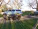 1900 Ford C-350 (Centurion Conversions) - A blue Chevrolet Suburban is parked next to a trailer, with a Dodge pickup truck visible in the background.