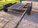1900 Ford C-350 (Centurion Conversions) - A dual axle trailer with a wooden deck is shown from a low angle, parked on a gravel surface.