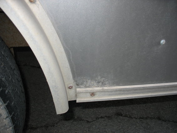 Trailer's metal side panel and wheel well with some corrosion visible