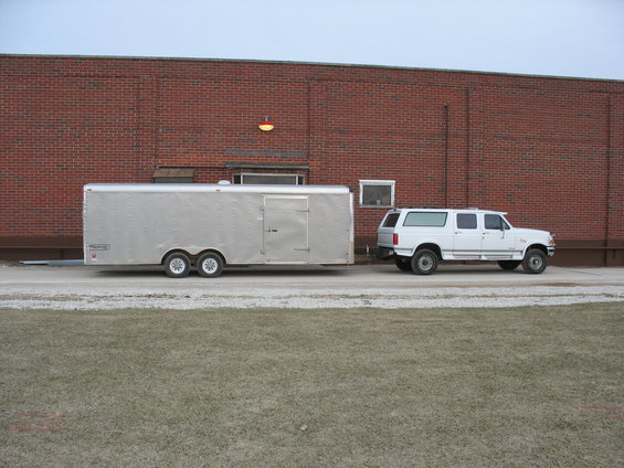 White Ford Bronco SUV towing a silver enclosed trailer, side view