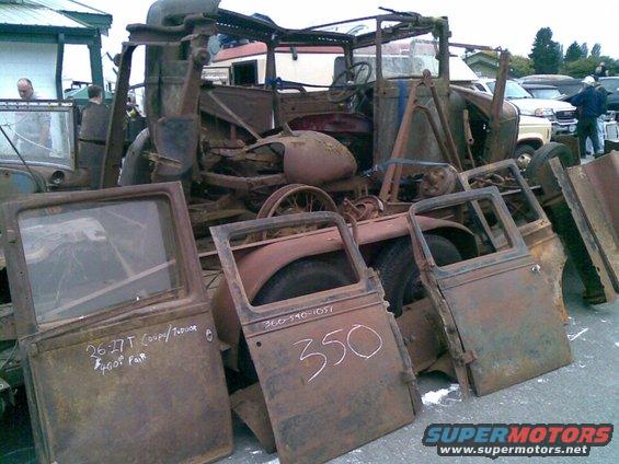 Pile of rusty car doors and a wrecked car body. One door says '26-27 T Coupe/Truck $400 Pair'. Another door has '350' written on it