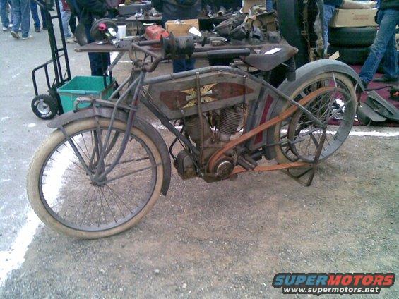 Antique motorcycle with a belt drive, wire wheels, and a weathered gray and red paint scheme