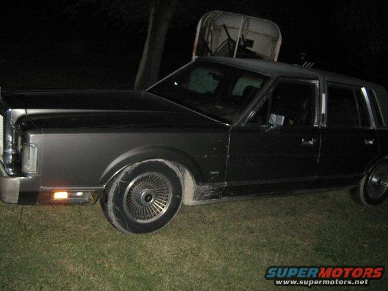 Dark sedan parked on grass at night. Has a chrome grille and distinct wheel covers