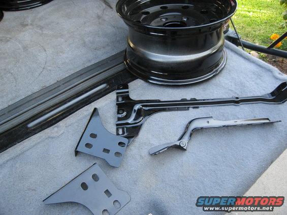 Black painted automotive parts including a steel wheel and brackets on a gray surface