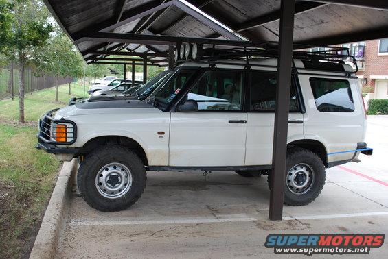 White 1999 Land Rover Discovery II parked under a carport, side view, with roof rack and off-road tires