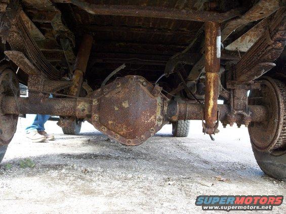 Heavily rusted truck rear axle, leaf springs, and shocks. A person stands in the background