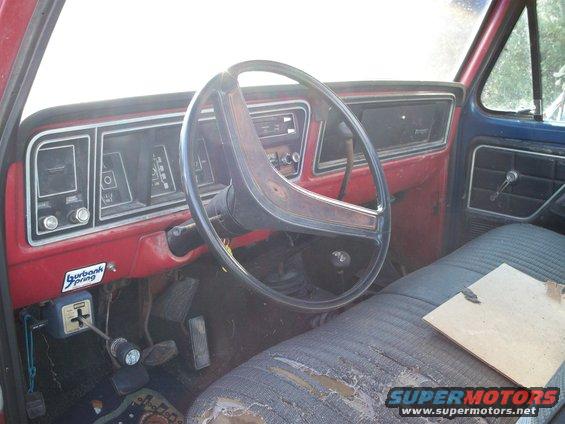Truck interior with worn blue and red dashboard, large steering wheel, and torn grey seat. A "Burbank Spring" sticker is visible