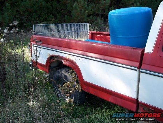 Rear view of a red and white 1988 Ford F-150 pickup truck bed with a blue barrel