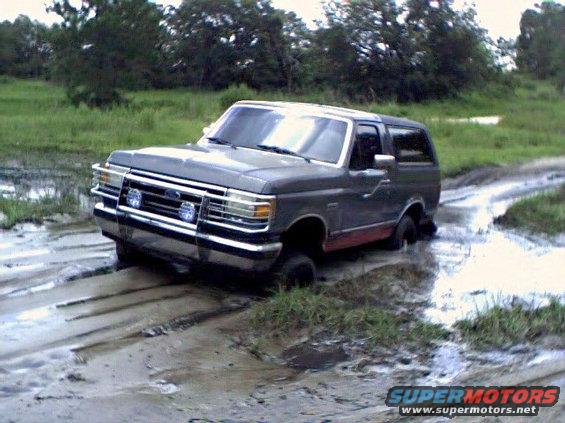 Gray Ford Bronco stuck in mud, front end visible, red lower body trim, chrome grille and bumper