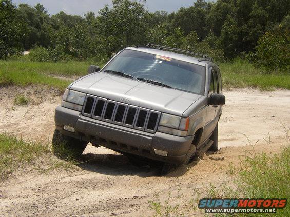 Silver Jeep Grand Cherokee stuck in sand on a dirt track, front wheel deep in sand