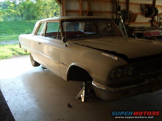 White 1963 Ford Galaxie sedan on jack stands in a garage, front 3/4 view