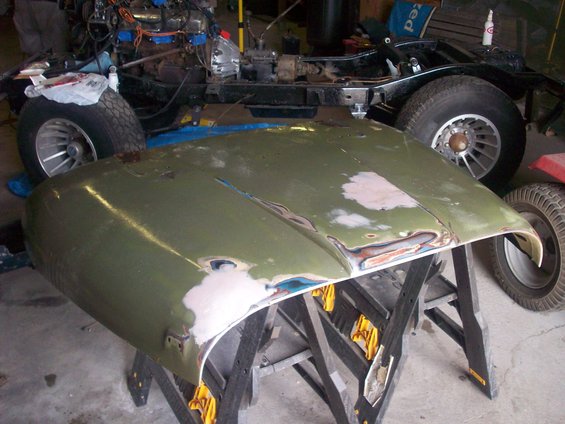 Green Jeep CJ5 hood with primer patches on sawhorses; vehicle chassis visible behind