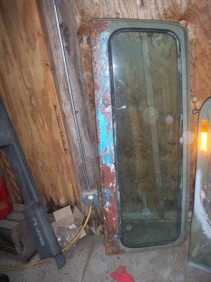 Jeep door with peeling blue and red paint over rust, and a green-tinted window