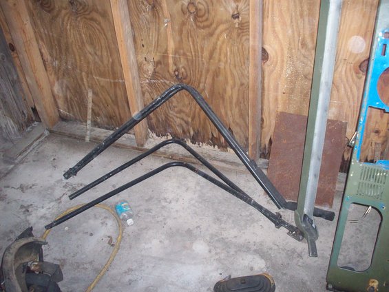 Black metal frame pieces, likely for a Jeep CJ5 roll bar, lying on a concrete floor