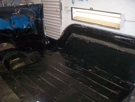 Interior floor and rear tub of a vehicle, coated in black protective material. A fluorescent light fixture is mounted on the wall above