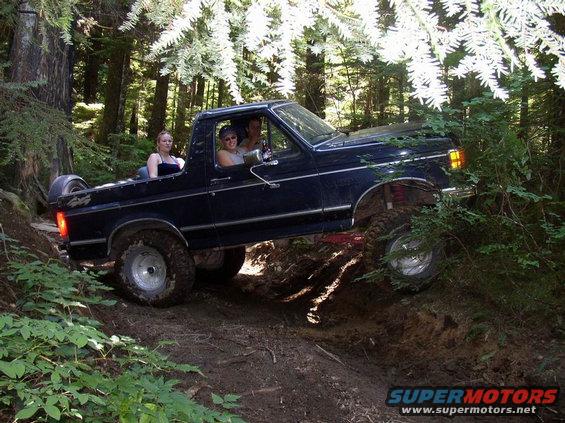 1988 Ford Bronco driving off-road with three people inside