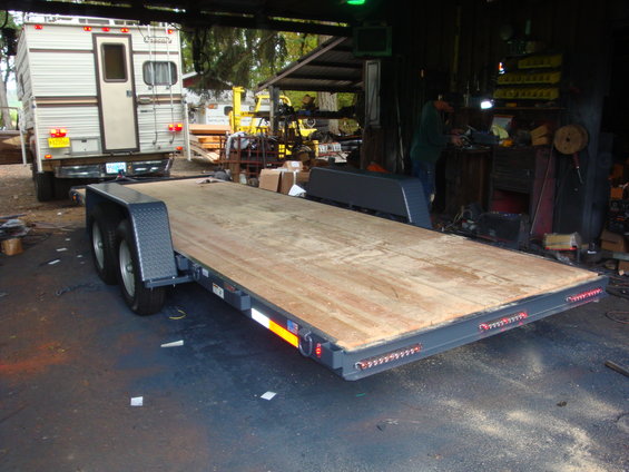 Car hauler trailer with wooden deck, dual axles, and a camper on a truck in the background