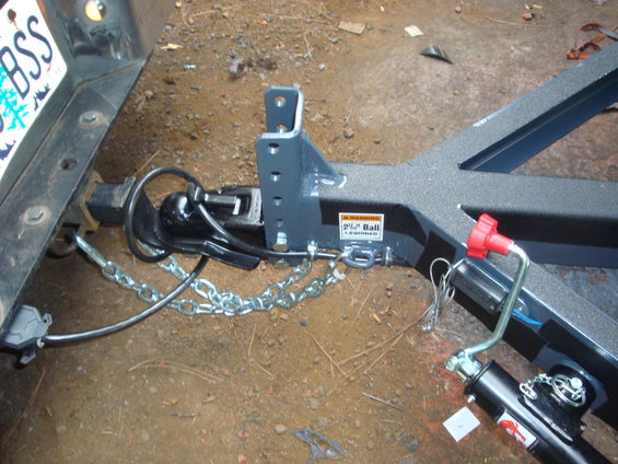 Trailer hitch assembly with coupler, safety chains, and wiring connector attached to a vehicle's receiver. A warning sticker indicates a 2-inch ball is required