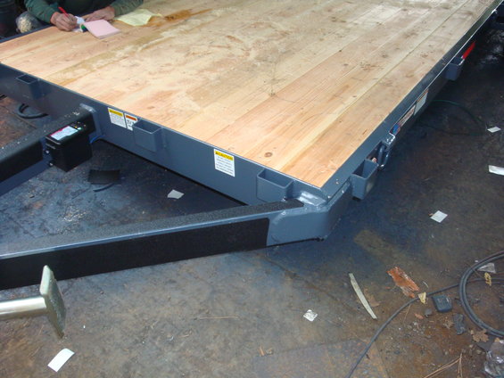 Trailer deck with wooden planks, metal frame, and a person writing on a notepad