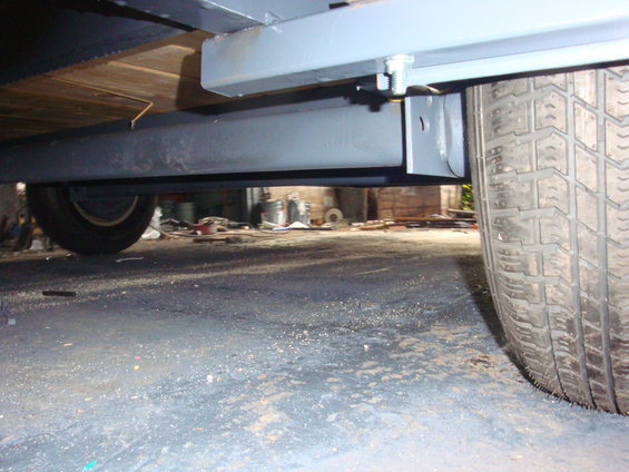 Close-up of trailer frame and tire. Wood planks visible above the frame