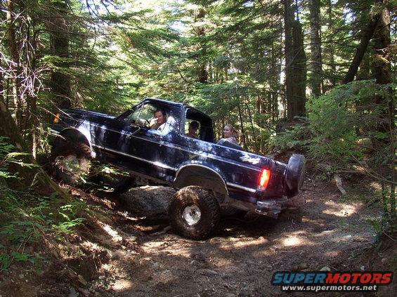 Dark blue Ford Bronco off-roading on a rocky, wooded trail