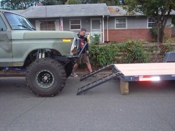 Olive green pickup truck with oversized tires and a trailer