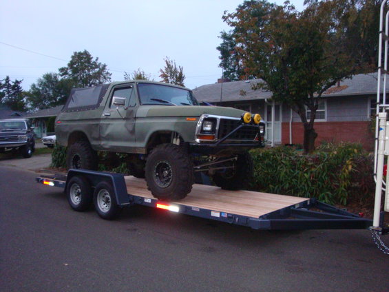 Green lifted Ford Bronco on trailer, front view with yellow fog lights