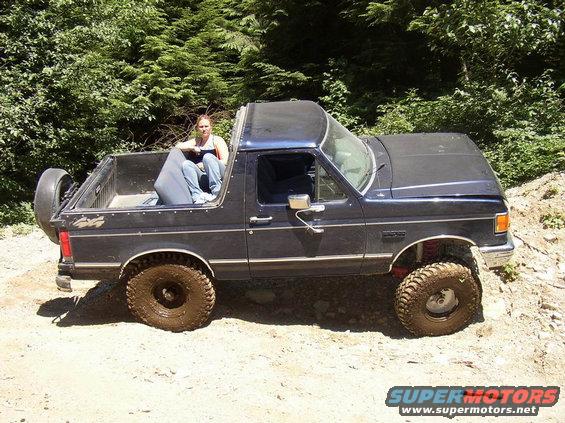 Dark blue 1987 Ford Bronco with off-road tires and a woman in the bed