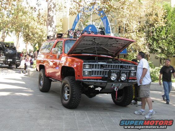 Orange SUV with hood open, lifted suspension, off-road tires, and roof rack