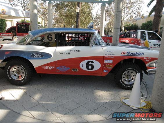 Side view of a heavily modified 1950s sedan with off-road tires and racing livery