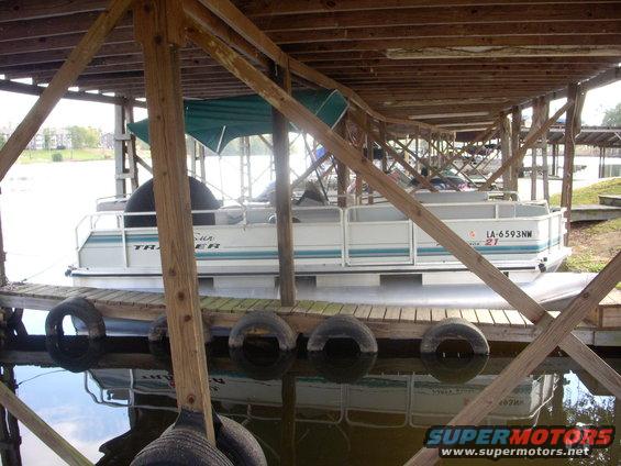 Pontoon boat with registration LA-6593NW docked under a wooden structure with other boats visible