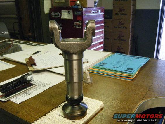 Driveshaft U-joint part on a wooden desk with papers and toolboxes in the background