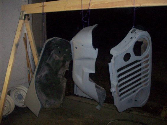 Three vehicle body panels hanging from a wooden rack, likely being prepped for painting