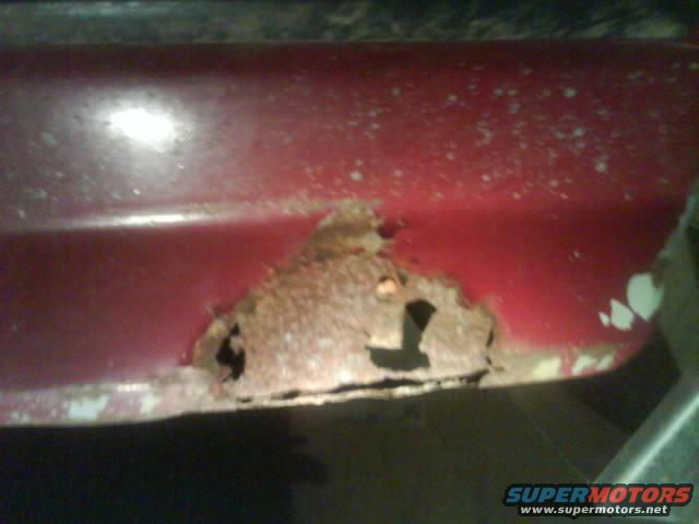 Close-up of red metal panel with significant rust damage and holes