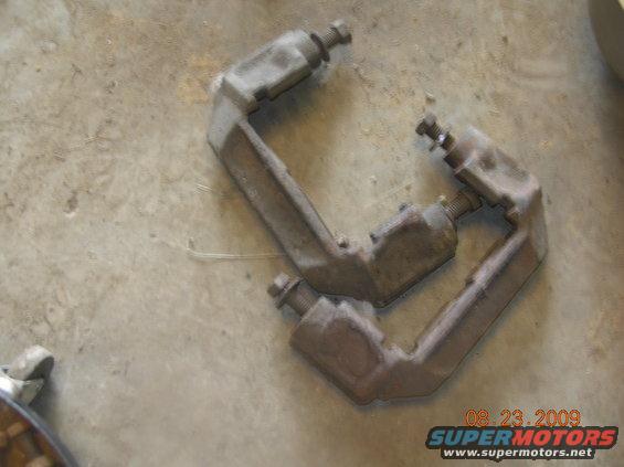Two rusty brake caliper brackets on a concrete surface
