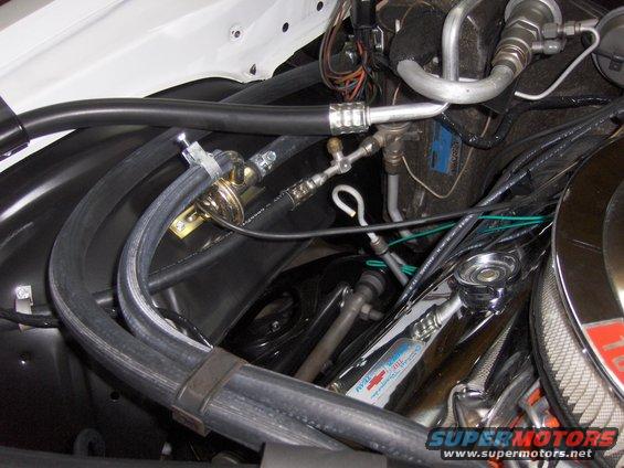 Close-up of engine bay hoses, AC lines, and some chrome parts. A small tag reads 'Chevrolet Performance Team'