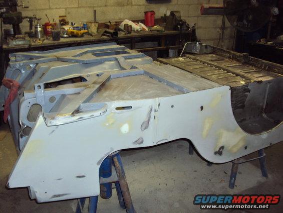 Jeep CJ body tub on sawhorses, undergoing repair with primer and body filler visible