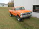 1975 Ford F-250 - This orange Ford F-250 pickup truck is parked on a grassy area next to a building with a large window.