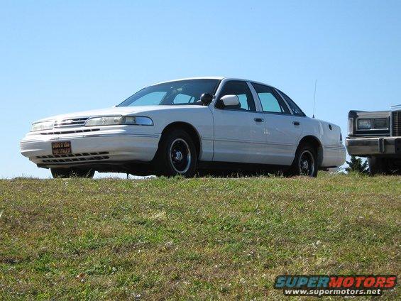 White 2000 Mercury Grand Marquis parked on a grassy hill, another vehicle partially visible to the right