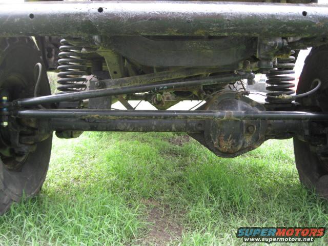 Underside view of a vehicle's suspension and drivetrain components, including springs, axles, and steering linkage