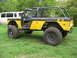 1973 Ford Bronco - Modified 1973 Ford Bronco with a roll cage and off-road tires sits in a grassy yard next to a white van.