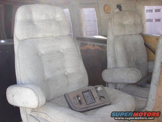 Interior shot of a van showing two plush captain's chairs with armrests and a center console with controls