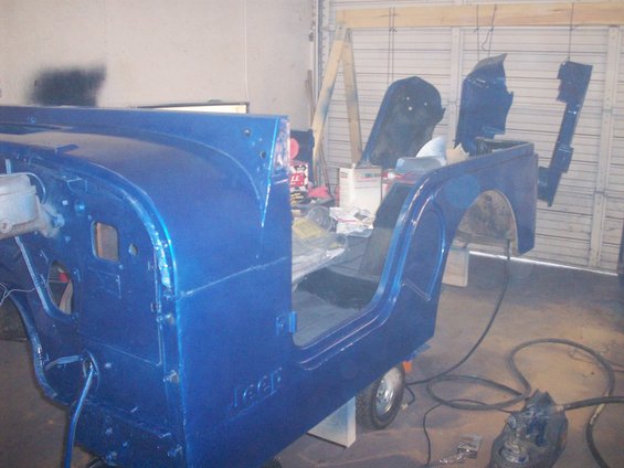 Blue Jeep CJ body in a garage, undergoing restoration, with doors removed and parts hanging