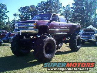 Maroon lifted pickup truck with oversized mud tires and dual exhaust stacks