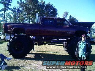 Monster truck with oversized tires and lifted suspension, a person stands next to the front wheel