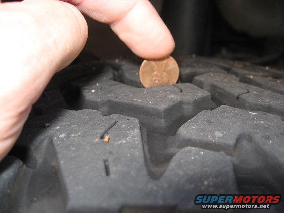 Tire tread depth measured with a penny, showing wear