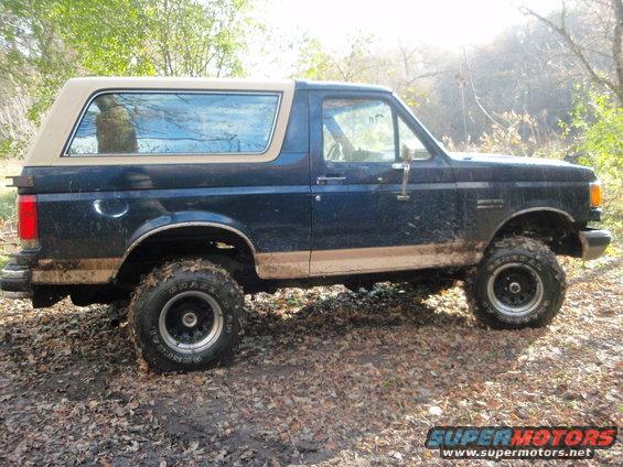 1990 Ford Bronco parked on a dirt path with fallen leaves