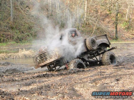 Old pickup truck with large tires stuck in mud, emitting smoke