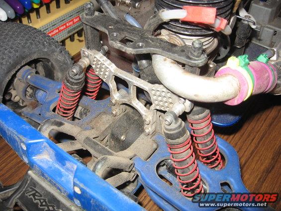Close-up of a remote control car's suspension and engine area. Shows red shocks, blue chassis, and exhaust pipe